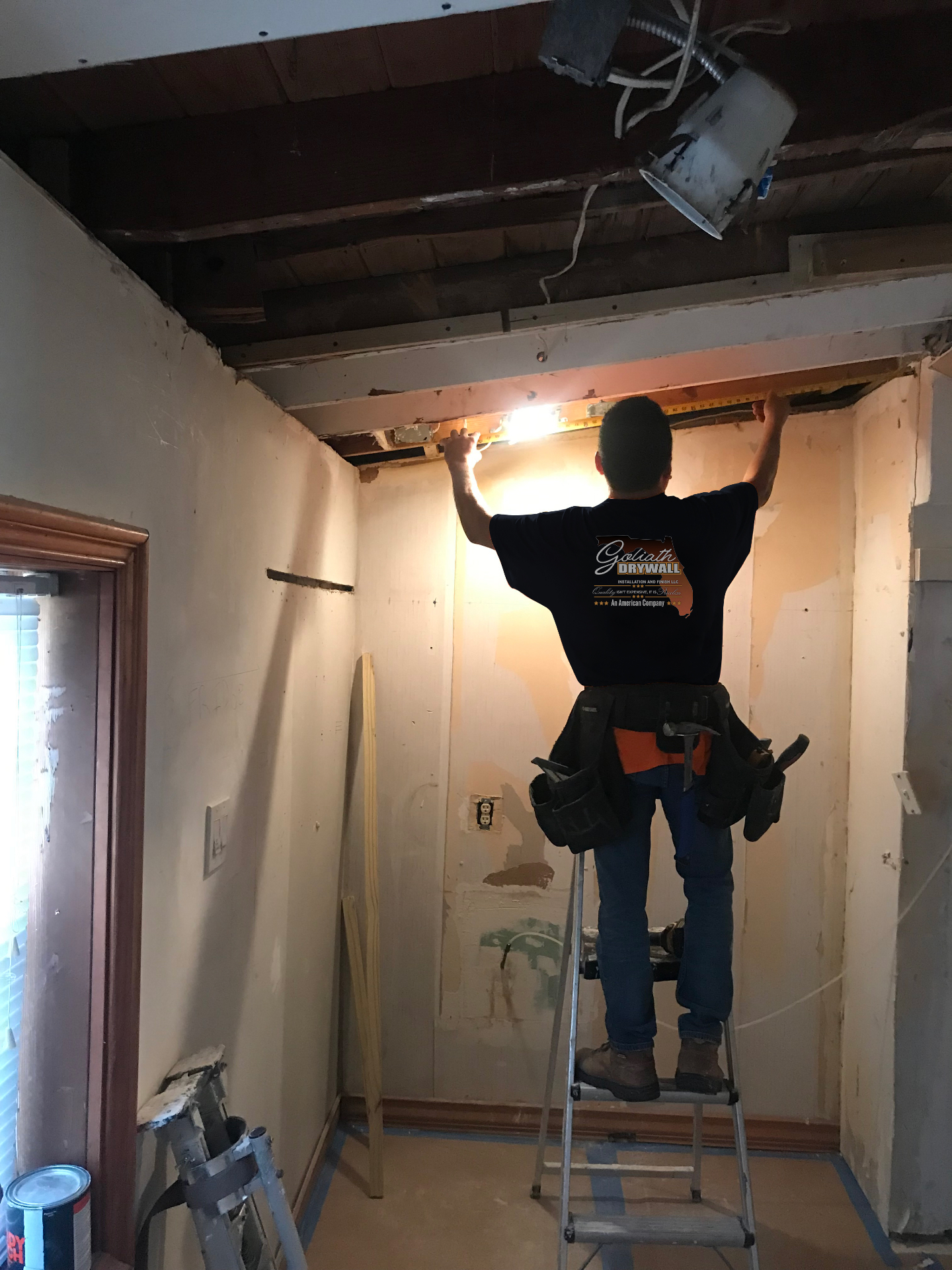 Crew member measuring ceiling framing during an interior repair