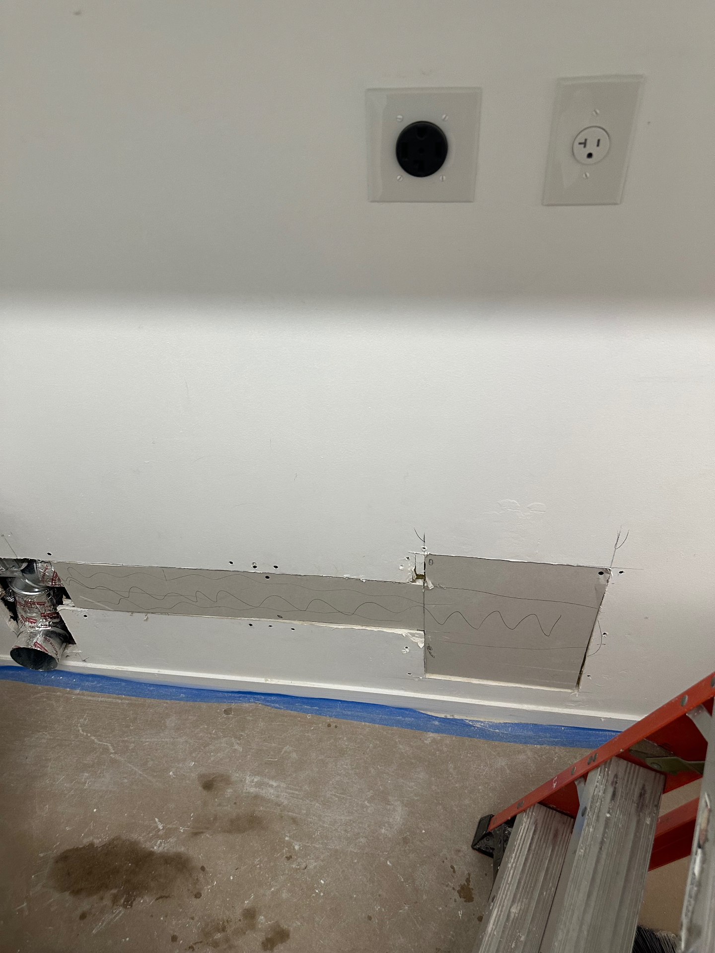 Laundry room wall with drywall patch behind dryer hookups before finishing