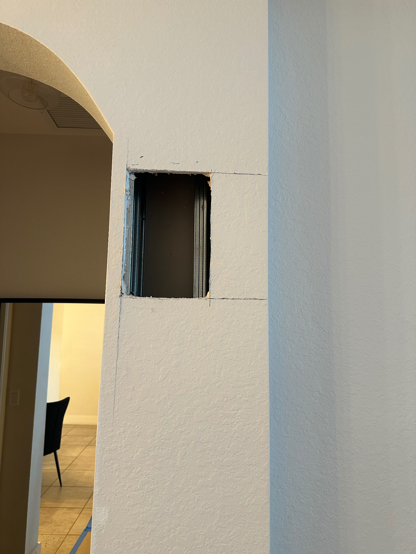 Square drywall cutout next to entryway arch exposing metal corner bead