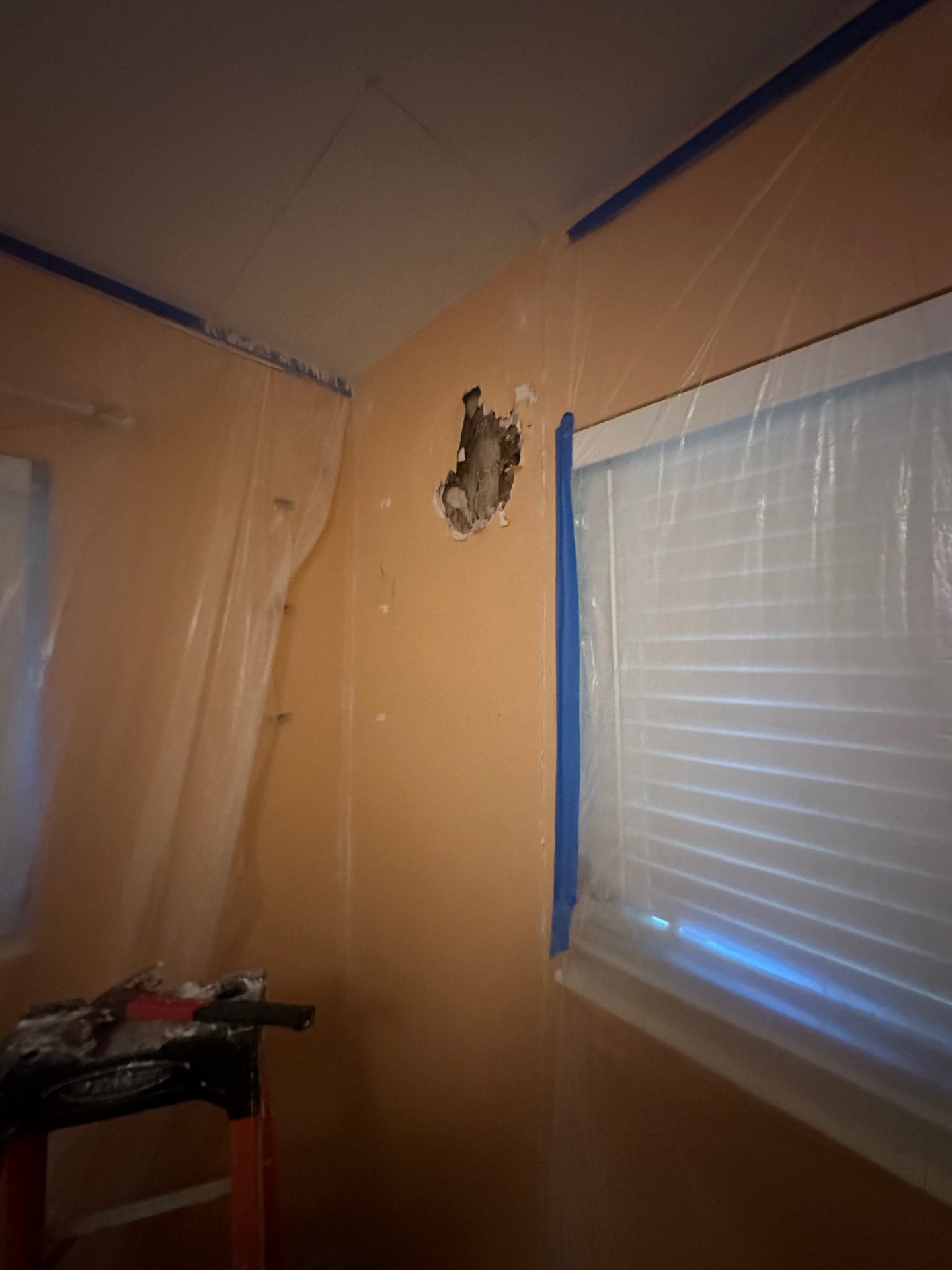 Bedroom wall with damaged hole near window, room masked off with plastic and tape